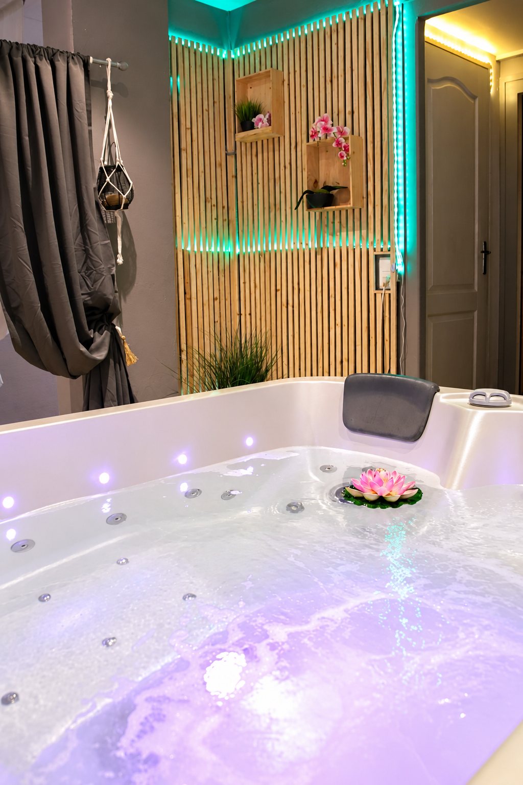 Une baignoire balnéo remplie d'eau avec une fleur de lotus flottante, éclairée de lumières violettes, devant un mur en lattes de bois avec rubans LED turquoise.